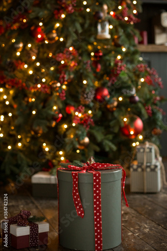 A beautifully wrapped New Year\'s gift on a wooden floor against the background of a Christmas tree with glowing lights. New Year and Christmas mood.