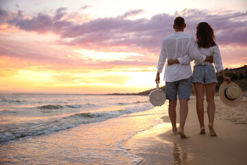 Wall Mural - Lovely couple walking on beach at sunset, back view. Space for text