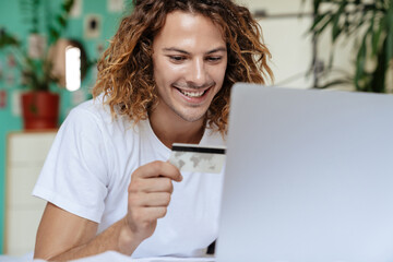 Caucasian handsome happy guy holding credit card and using laptop