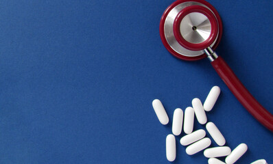 Wall Mural - Red stethoscope and white pills isolated on blue background. Medicine concept. Copy space