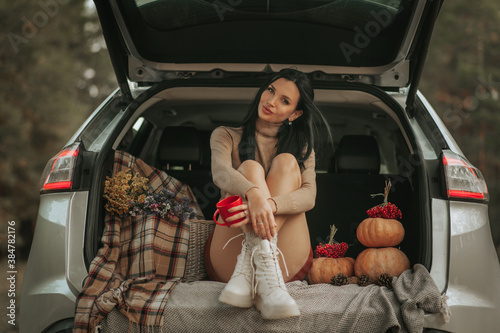 Love Coffee! Young woman holding red mug and drinking coffee in car in fall season. Girl relaxing and enjoying sunset traveling on car. Travel, road trip autumn fashion concept