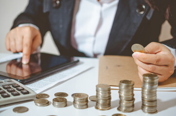 Closeup image businesswoman holding coins putting to stacking coins bank and calculating. concept saving money wealth for finance accounting.