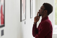 Side View Portrait Of Young African-American Man Looking At Paintings And Thinking At Art Gallery Or Museum Exhibition, Copy Space