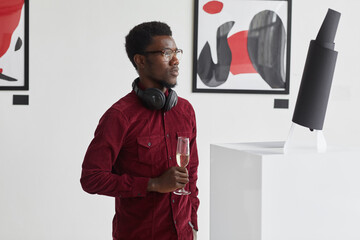 Wall Mural - Waist up portrait of modern African-American man holding champagne glass while exploring modern art gallery exhibition, copy space