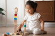 © fizkes - Close up pretty little Asian girl playing wooden cubes and toy dinosaurs alone, sitting on warm wooden floor with underfloor heating, cute adorable toddler child having fun at home