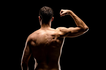 Wall Mural - Strong muscular man showing biceps back view, isolated on black background.