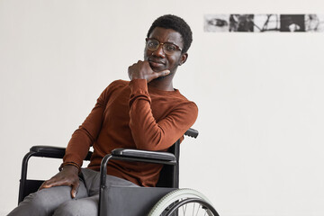 Minimal portrait of young African-American man using wheelchair and looking at camera while posing in modern art gallery, copy space