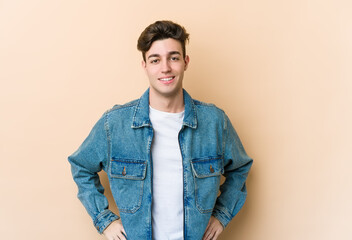 Wall Mural - Young caucasian man isolated on beige background confident keeping hands on hips.