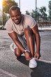 © Afshar Tetyana - Joyous man fixing his loose shoelaces on a sports court