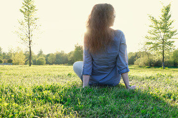 Wall Mural - Young woman sitting on the grass. Golden sunset in the background.