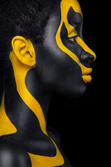 Wall Mural - Face art. Woman with black and yellow body paint. Young african girl with colorful bodypaint. An amazing model with yellow makeup. Closeup face.