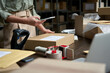 © insta_photos - Female small business owner using mobile app on smartphone checking parcel box. Warehouse worker, seller holding phone scanning retail dropshipping package postal parcel bar code on cell technology.