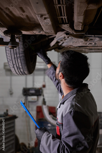 young caucasian auto mechanic in uniform is examining car wheels in auto service. male is concentrated on work