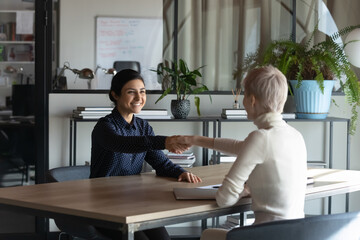 Wall Mural - Happy diverse female colleagues or partners shake hands get acquainted greeting at meeting in office. Smiling multiracial businesswomen handshake close deal or make agreement. Recruitment concept.