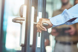 Male hand opening glass door in the modern office, close up shot