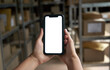 © insta_photos - Female warehouse worker, small stock business owner holding cell phone in hands mock up screen ad checking retail package parcels for commercial shipping boxes delivery using mobile app on smartphone.