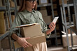 © insta_photos - Female warehouse worker manager, small stock business owner holding phone and retail package parcel boxes checking commercial shipping delivery order on smartphone using mobile app technology.