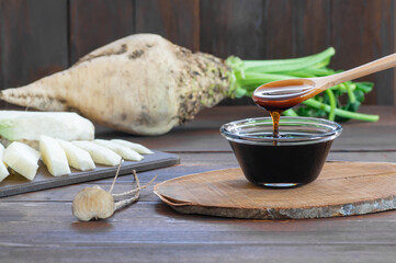 Sugar beet molasses in glass bowl with fresh sugar beetroot plant, healthy food, beta vulgaris