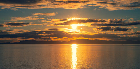 Sunset over the ocean water with the Alaskan Coast in silhouette