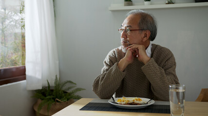 Sad old retired gray haired grandpa asian man sitting alone at table desk at window boring stay home self isolation quarantine feeling depress in problem mental health.