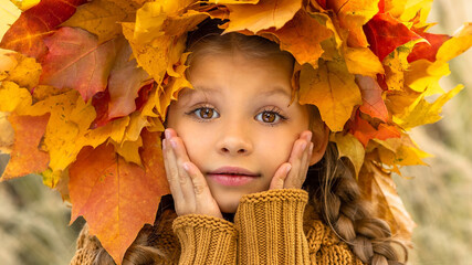 Wall Mural - A little girl in a sweater and a maple wreath on her head in autumn.