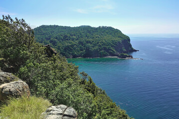 In the foreground is a mountain slope with large stones. A green island is visible in the turquoise Andaman Sea. Clear azure sky. Thailand. Summer.
