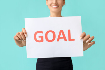 Young businesswoman holding paper with word GOAL on color background