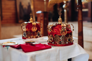 Picture of two beautiful crowns with gold and red cloth stand on a table with other attributes in the church before the baptis