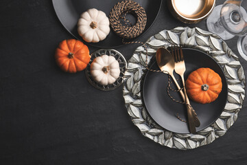 autumn table setting with golden cutlery and pumpkins on black background, flat lay. space for text