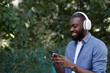 © YURII MASLAK - Portrait of smiling guy in earphones and mobile phone outdoors. Young Afro-American man in headphones listening music on smart phone using music app. Walking in the street, relaxation, leisure.
