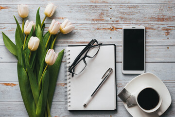Wall Mural - White bouquet of tulips on wooden background with coffee Cup, a smartphone and an empty notebook