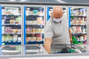 A man in a medical mask in the frozen food section of a supermarket. Coronavirus pandemic.