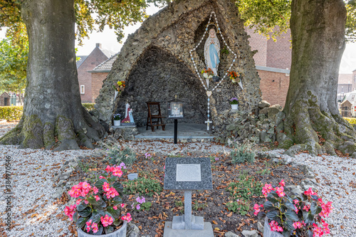 Fotografía Replica of Our Lady of Lourdes surrounded by a huge rosary and the statue of Bernadette praying to Our Lady, pink flowers and an information pole in the foreground