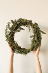 Wall Mural - Female hands holding round wreath frame made of fir and eucalyptus branches on neutral background. Christmas / New Year celebration decoration. Holiday concept.