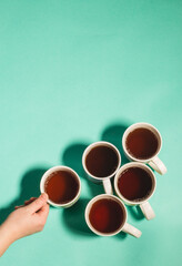 Different mugs of hot drinks - tea, coffee on a light green background top view, vertical. The woman hand holds one of the mugs of tea or coffee