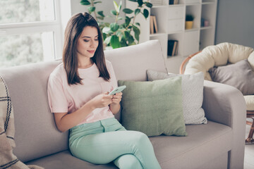 Sticker - Photo portrait of woman holding phone in two hands sitting on sofa with crossed legs indoors