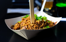A Recyclable Cardboard Plate With Asian Food Inside, Noodles, Chicken, Vegetables ... And Nailed To It, Some Chopsticks To Eat And On The Other Side, A Classic Western White Plastic Fork