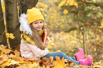 Wall Mural - A little girl is sitting on the ground in the autumn forest.