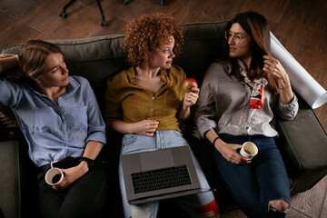 Wall Mural - Girlfriends talking and laughing in office. Beautiful women drinking coffee in the office.