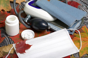 Wall Mural - Tonometer for measuring blood pressure. Next to a container with pills and a medical mask. Among the autumn maple leaves.