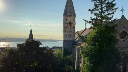 Wall Mural - Old vintage medievel stone church building surrounded with trees and a cross on top of the roof with a chime tower. İstanbul Bosphorus at the background and ships