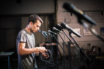 Theater audio technician adjusting an microphones on the scene. Installing and testing the sound system in the background