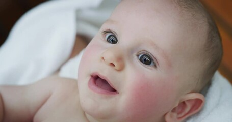 Wall Mural - Authentic close up shot of a cute newborn baby in a white bathrobe is having fun with his mother after bathing and smiling. 