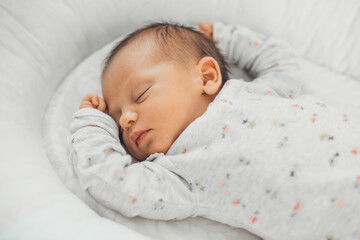 upper view photo of a caucasian newborn baby sleeping in white clothes at home
