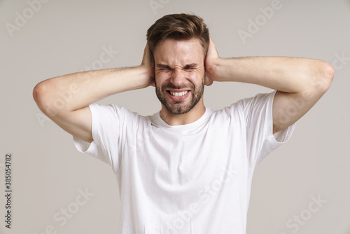 Fotomural Stressed handsome unshaven guy grimacing and covering his ears