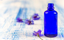 Essential Oil Bottles On Medicinal Cornflowers Centaurea Cyanus Bachelor's Button Flowers And Herbs Background,