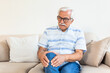 © Graphicroyalty - Elderly man sitting on a sofa at home and touching his knee by the pain.