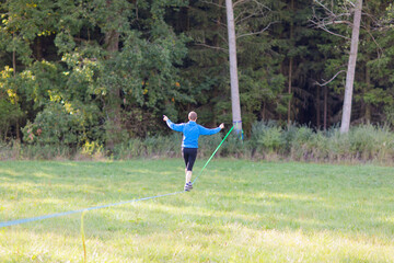 Wall Mural - Young man balancing and jumping on slackline. Man walking, jumping and balancing on rope in park
Sports a tightrope or slackline outdoor in a city park in summer slacklining, balance, training concept