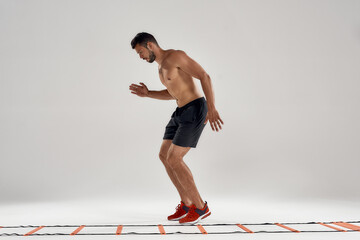 Wall Mural - Train your body. Full length shot of young athletic man training on agility ladder drill isolated over grey background