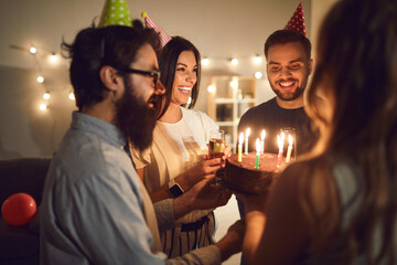 Group of smiling friends presenting birthday cake to their friend